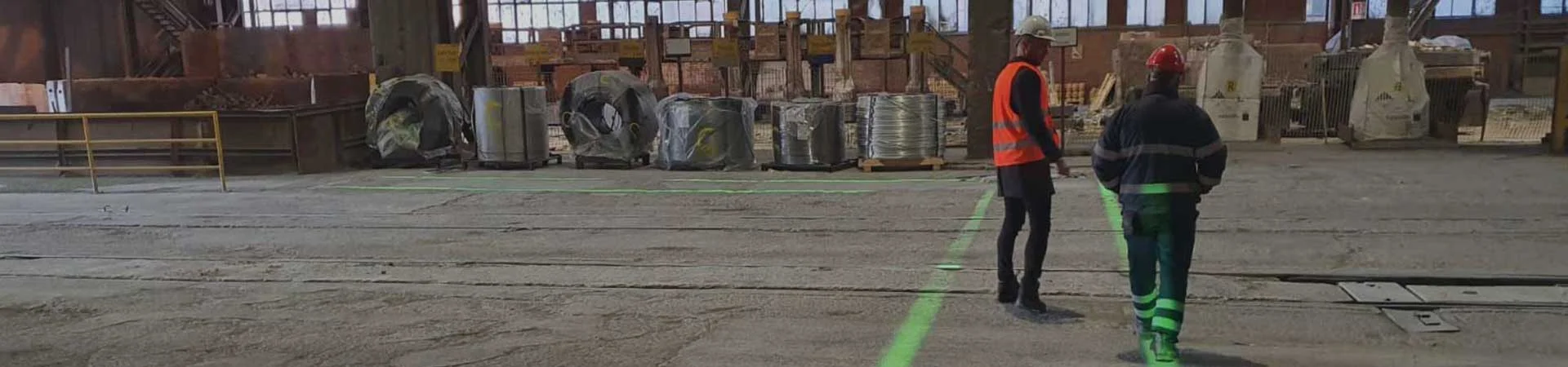 Two warehouse workers in protective gear standing by a safety projector line for laser walkways.